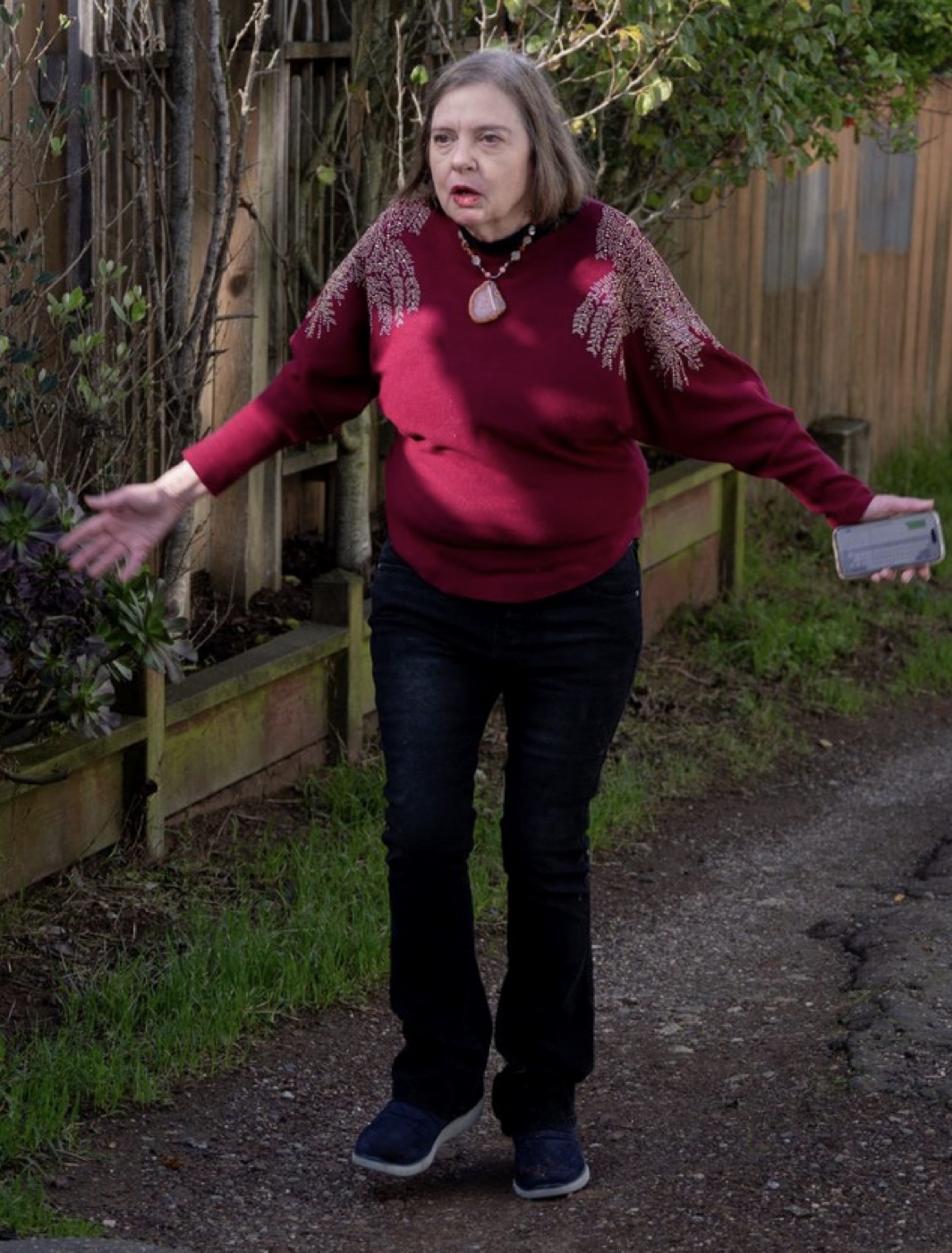 A person in a red sweater shrugging with both arms out.
